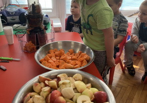 Dziecko wkłada marchewkę i jabłko do sokowirówki.