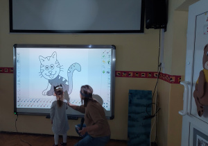Dziewczynka koloruje kota na tablicy multimedialnej.