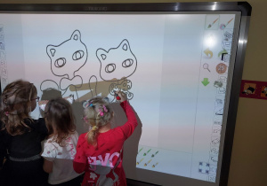 Dzieci kolorują koty na tablicy multimedialnej.