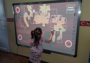 Dziewczynka układa puzzle na tablicy multimedialnej.