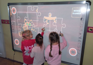 Dzieci układają puzzle na tablicy multimedialnej.