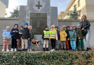 Dzieci zapalają znicze przy tablicy upamiętniającej poległych żołnierzy żołnierzy