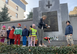 Dzieci zapalają znicze przy tablicy upamiętniającej poległych żołnierzy żołnierzy