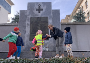 Dzieci zapalają znicze przy tablicy upamiętniającej poległych żołnierzy żołnierzy